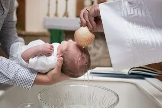 Ein Baby wird mit Wasser aus einer Muschel getauft.