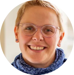 Lächelnde Frau mit kurzen blonden Haaren und Brille.