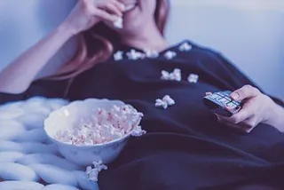 Eine Person isst Popcorn und hält eine Fernbedienung.