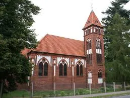 Kleine rote Backsteinkirche mit Turm und orangefarbenem Dach.