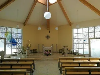 Modernes Kircheninneres mit Holzbänken und abstraktem Buntglas.