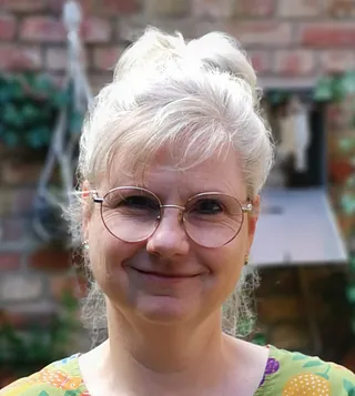 Lächelnde Frau mit grauen Haaren und runder Brille.