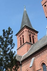 Roter Backsteinkirchturm mit Kreuz.