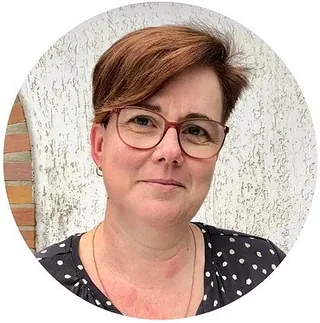 Lächelnde Frau mit kurzen braunen Haaren und Brille.