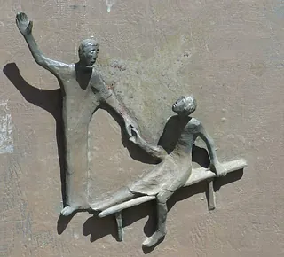  Bronzerelief einer Person, die einer anderen hilft.