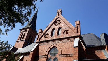 Kirchturm und Dach der St. Otto Kirche vor einem klaren blauen Himmel.
